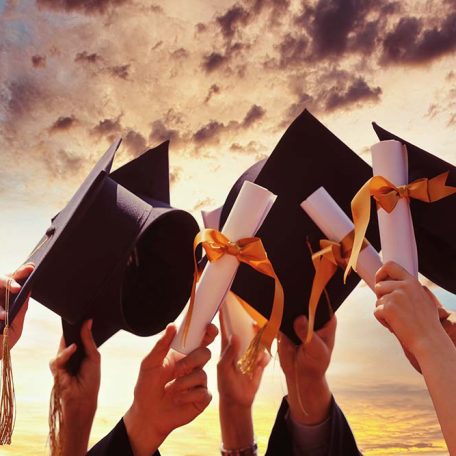Graduation people concept - a group of happy international students in mortar boards and bachelor gowns with diplomas.